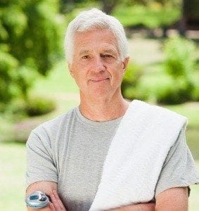 A man is in a sunny park ready to go jogging and is looking at the camera